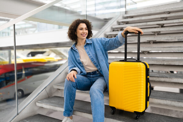 Beautiful Young Woman With Luggage Sitting On Stairs At Airport