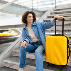 Beautiful Young Woman With Luggage Sitting On Stairs At Airport