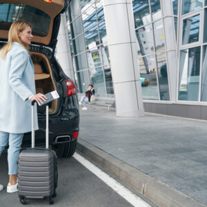 Passenger With Travel Document And Baggage Near Open Car Trunk