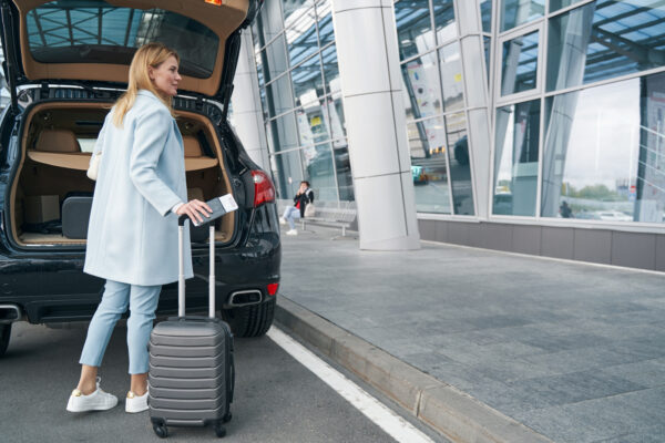 Passenger With Travel Document And Baggage Near Open Car Trunk